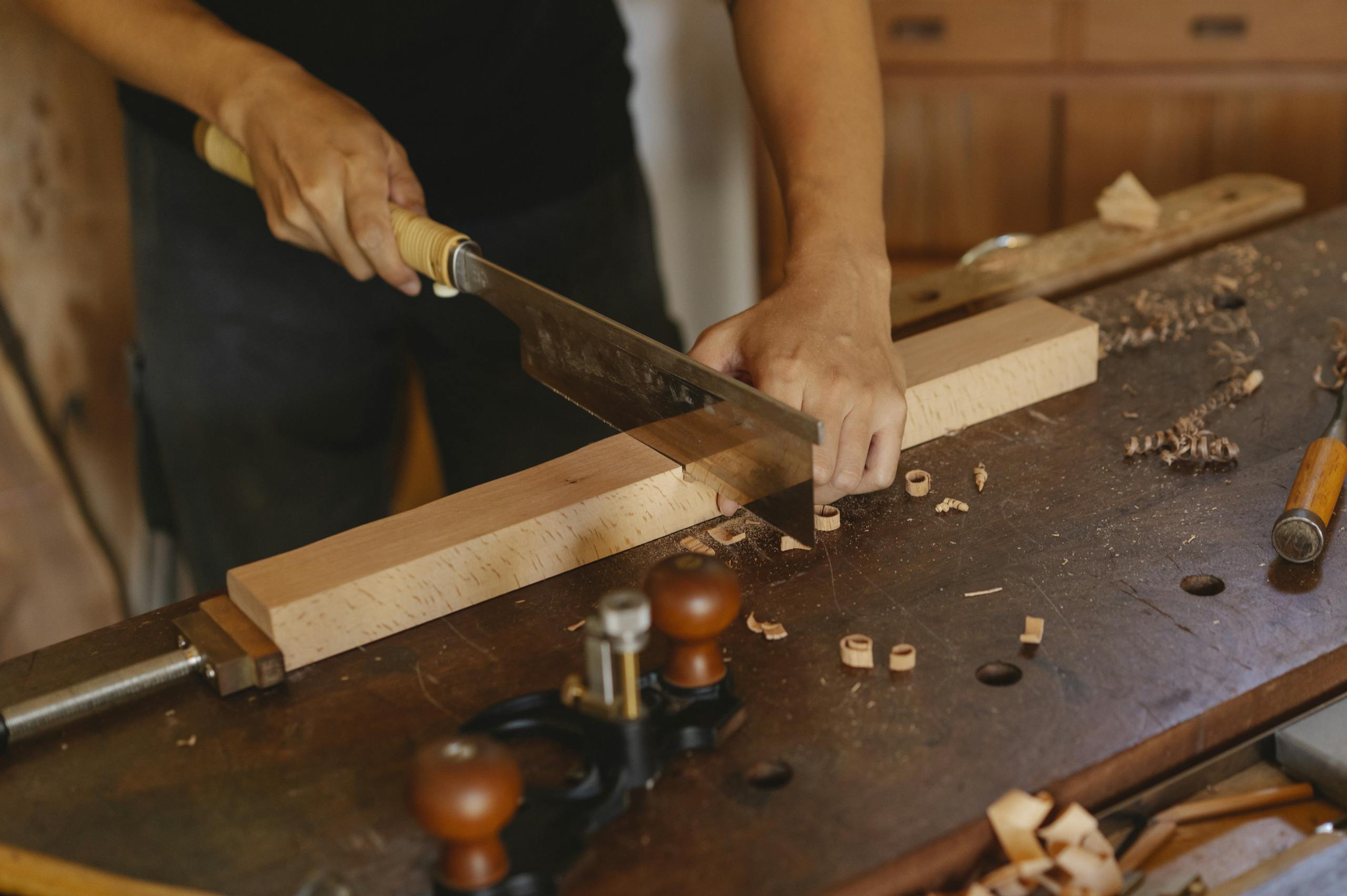 A carpenter uses a saw to skillfully cut a wooden plank in a workshop.