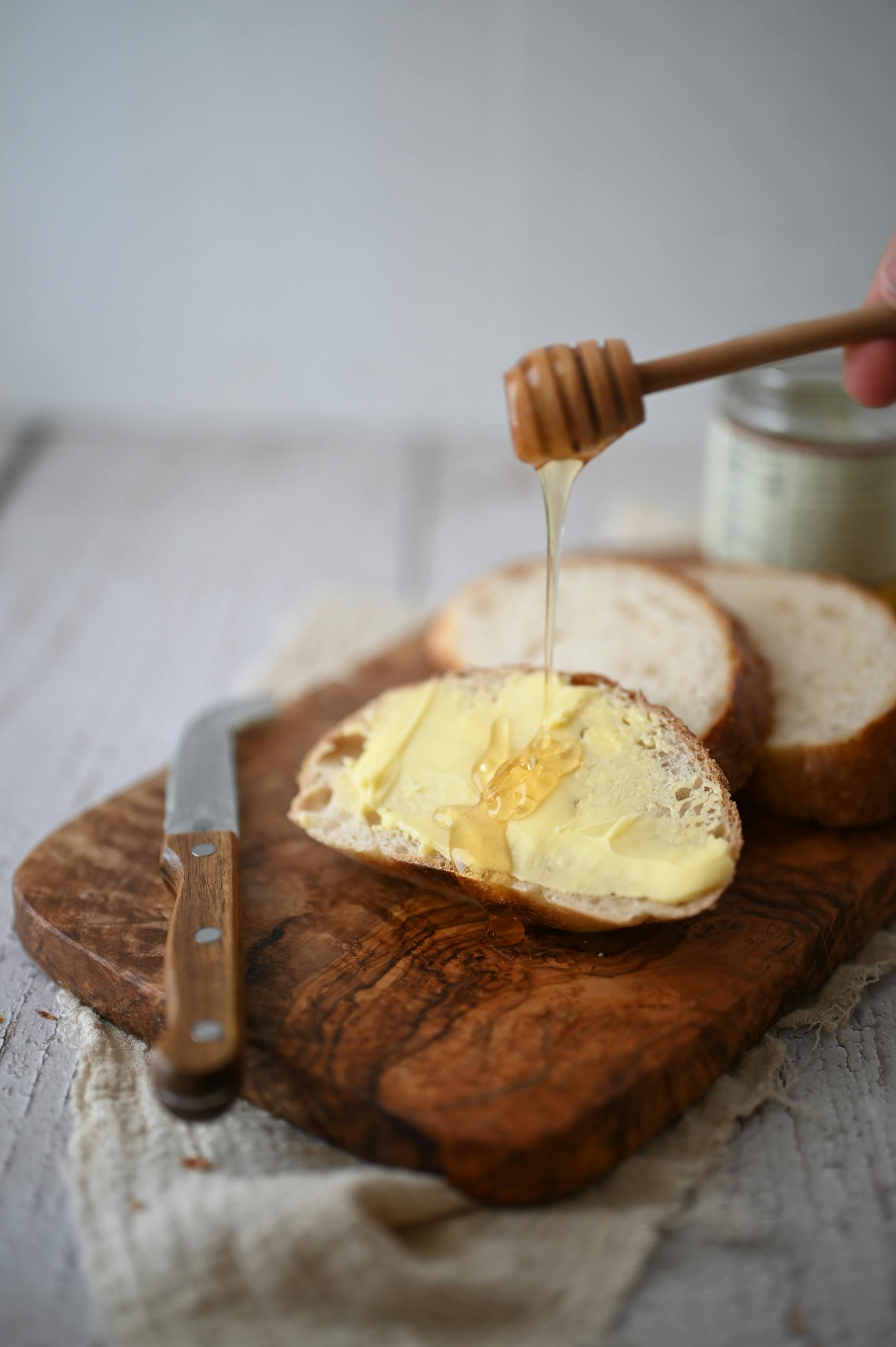 Close-up of bread slice with butter and honey on a wooden cutting board.