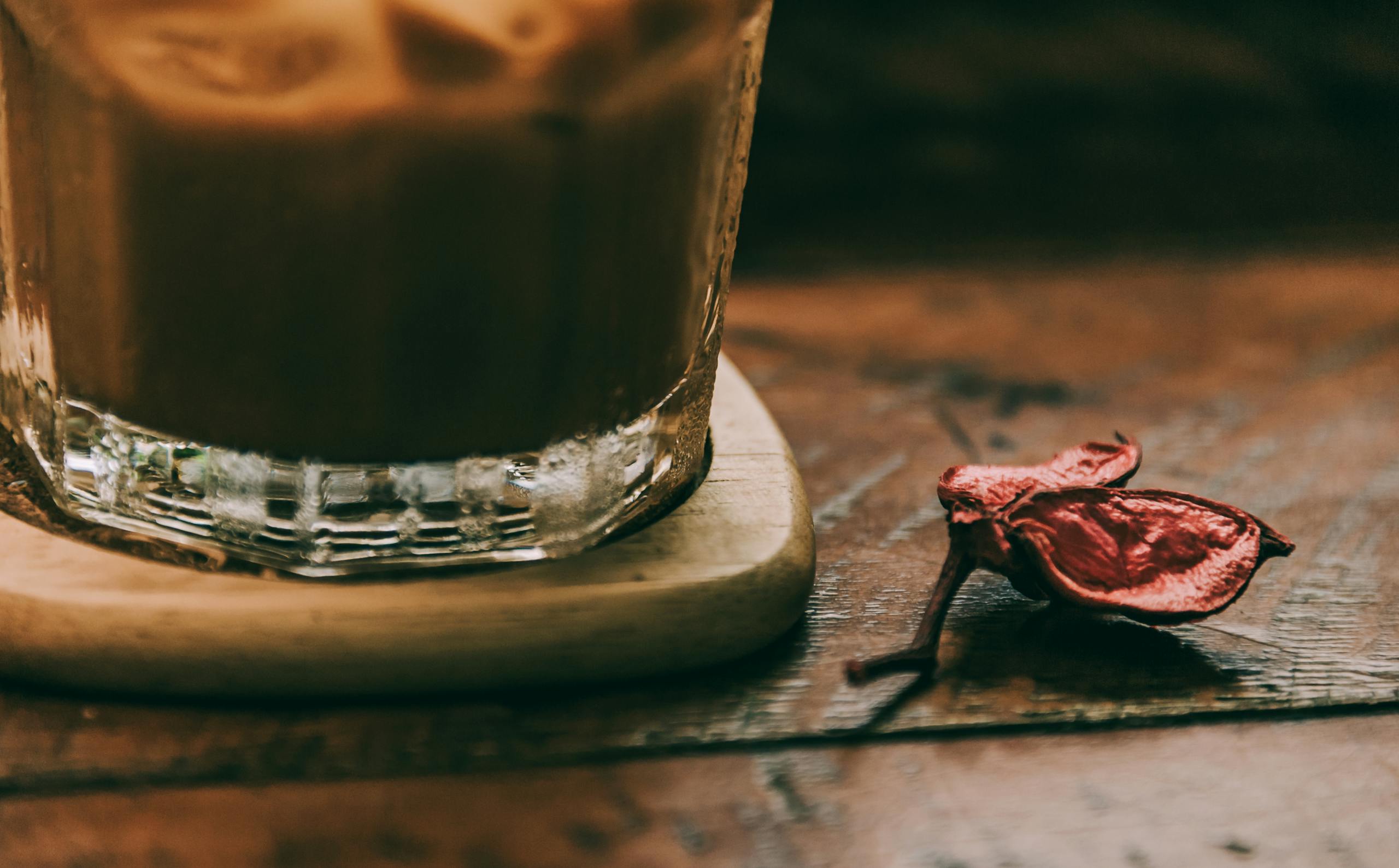 Close-up of iced coffee with a dried flower on a rustic wooden table. Warm and inviting mood.