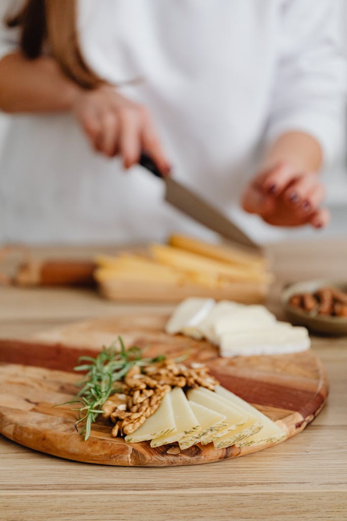 A cheese platter with walnuts and rosemary being prepared on a wooden board.