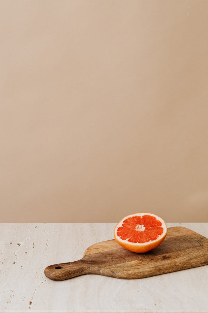 A halved grapefruit on a wooden cutting board with beige background, showcasing freshness.
