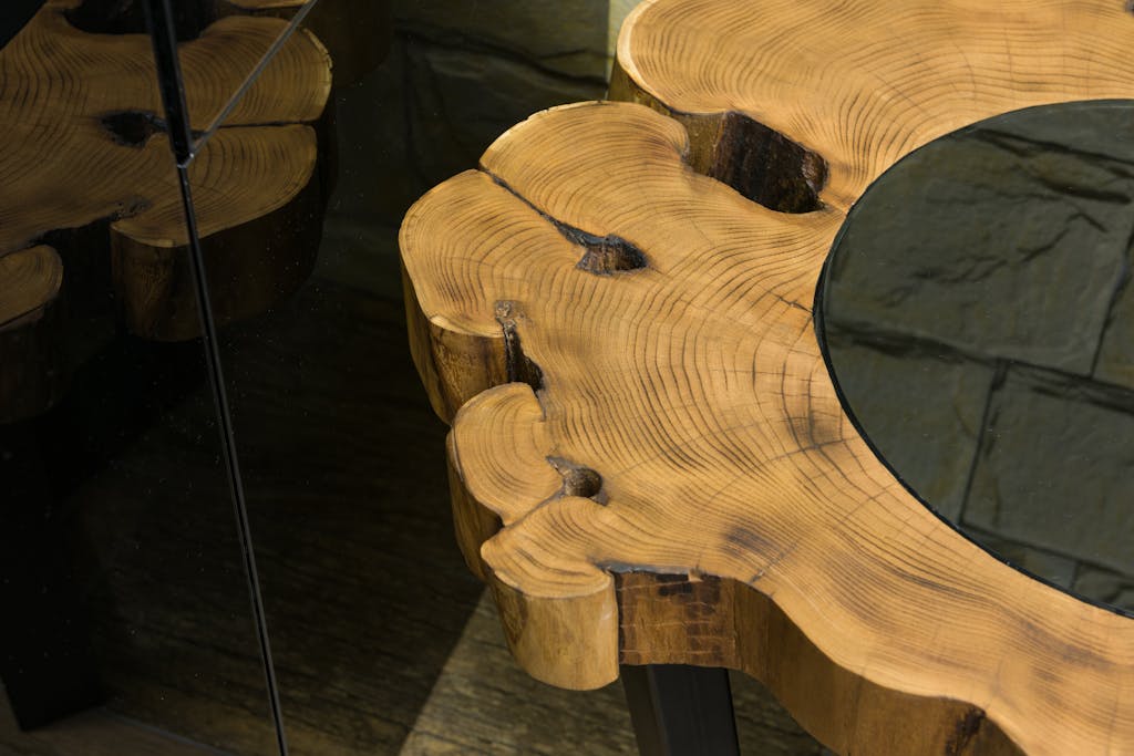 A rustic wooden table featuring organic contours and a reflective glass surface.