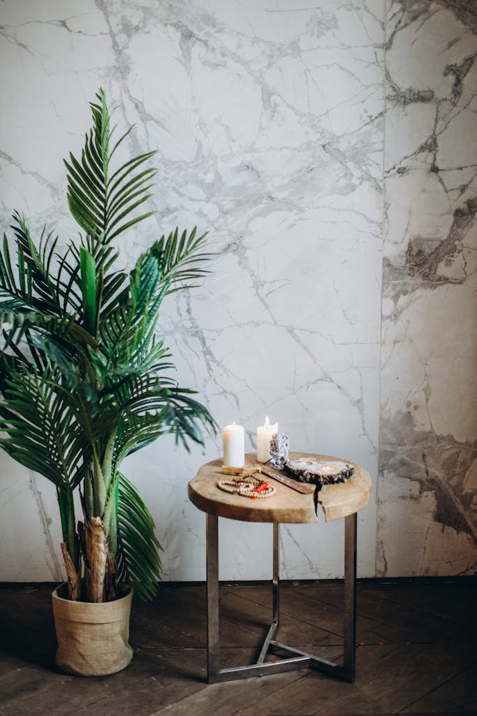 A serene indoor decor scene featuring candles, a potted plant, and prayer beads on a wooden table.