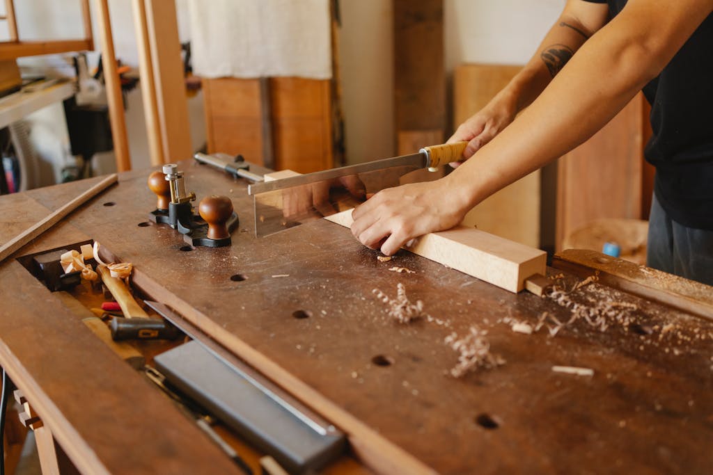 A skilled carpenter using a handsaw to cut timber on a workbench in a well-equipped workshop.