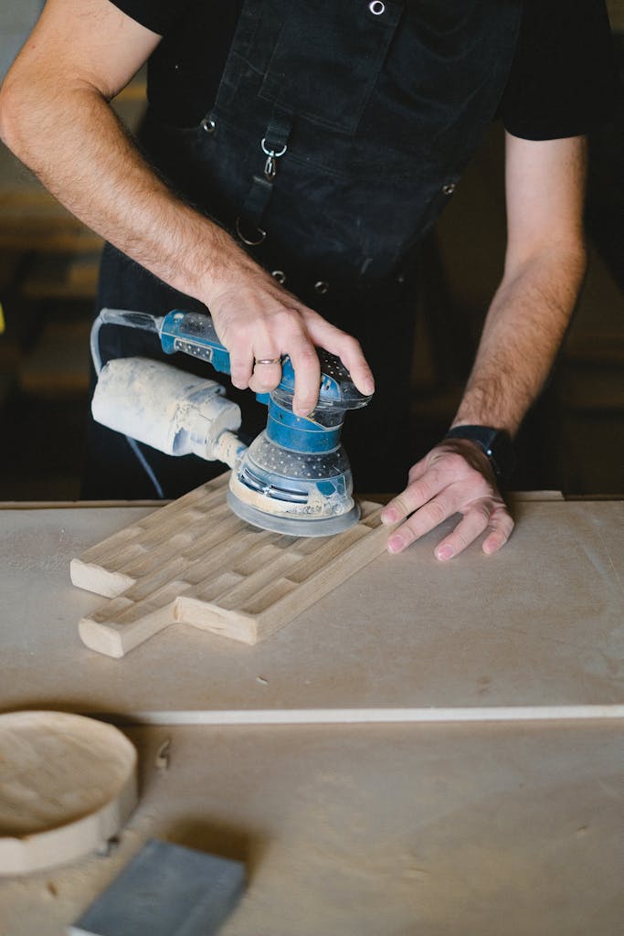 A skilled craftsman uses an electric sander on a wooden board in a workshop setting.
