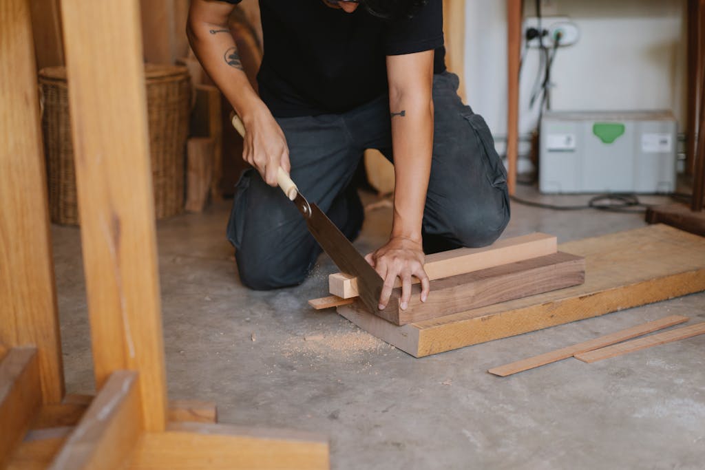 A skilled craftsman using a hand saw to cut wooden planks in an indoor workshop setting.