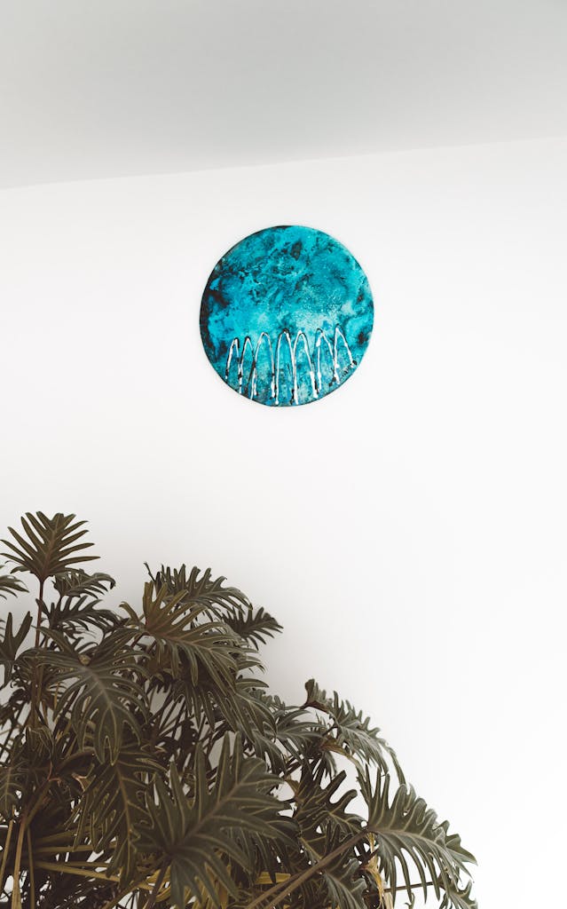 Abstract wall art with turquoise circle and plant in a minimalist indoor setting.