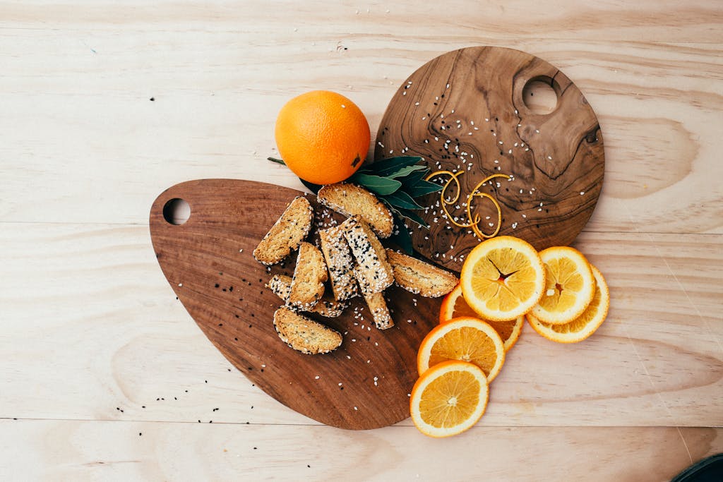 Artistic flatlay of biscotti with orange slices and sesame seeds on wooden boards.