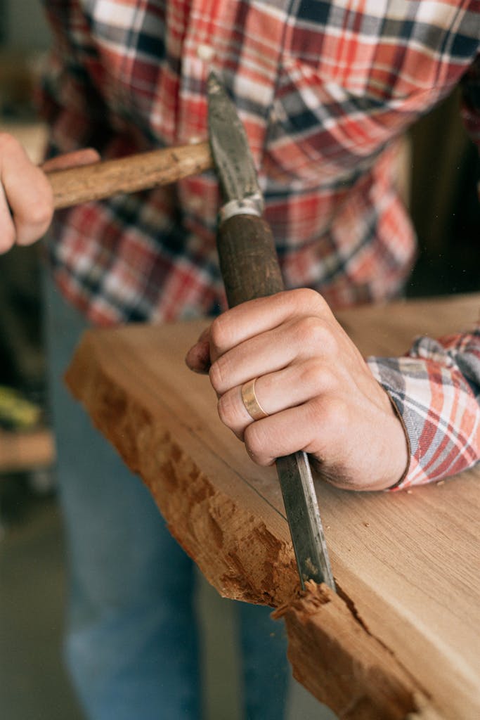 Close-up of a craftsman skillfully carving wood with a chisel in a workshop.