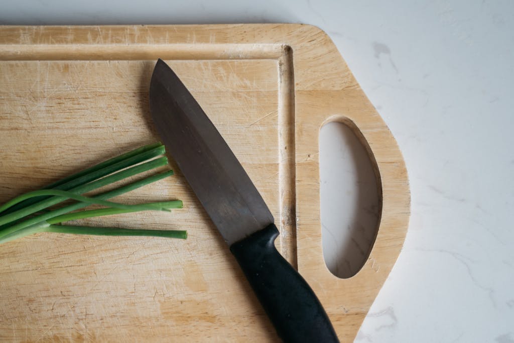 Close-up of a knife on a wooden cutting board with green onions. Ideal for kitchen and cooking themes.