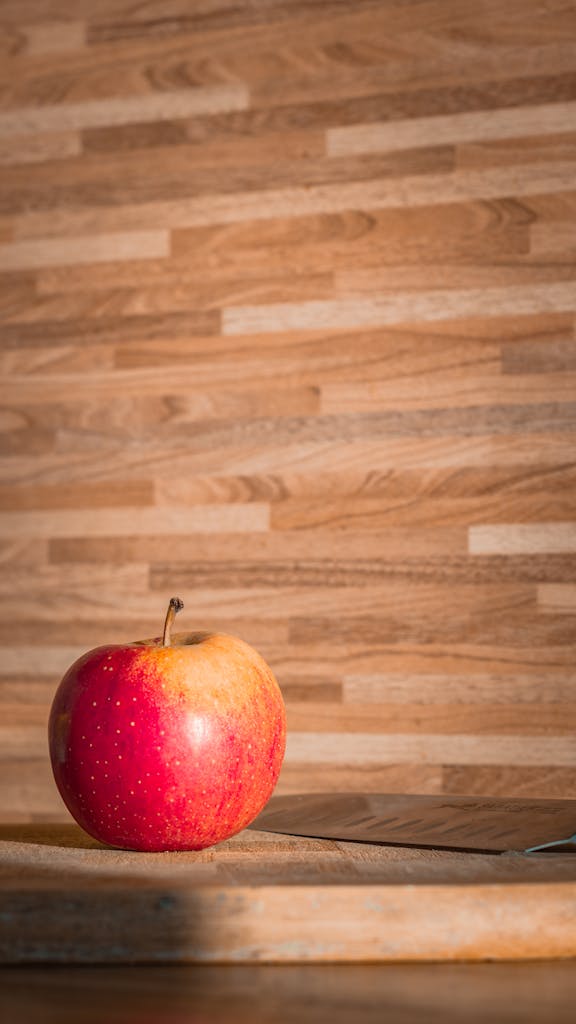 Close-up of a vibrant red apple on a wooden cutting board with warm lighting.