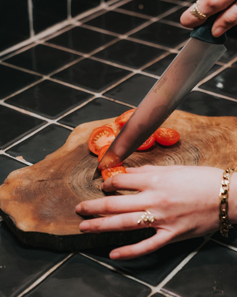 Close-up of a woman slicing tomatoes on a rustic wooden cutting board in a kitchen setting.