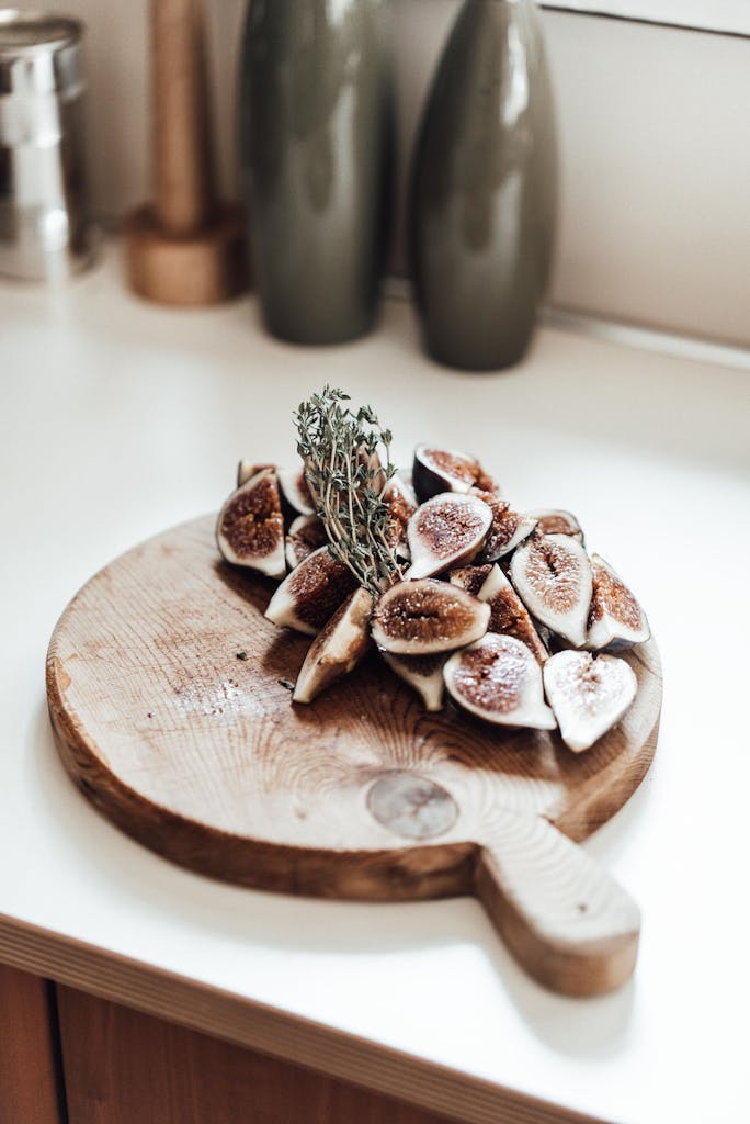 Close-up of freshly sliced figs with thyme on a wooden cutting board in a kitchen setting.