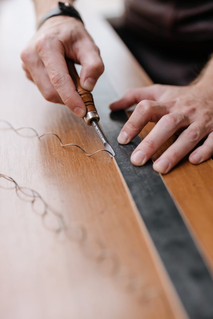 Focused shot on hands using a chisel and ruler to intricately engrave designs on a wooden surface.