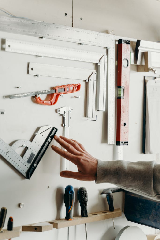 Hand selecting tool from well-organized carpentry wall display. Ideal for woodworking content.