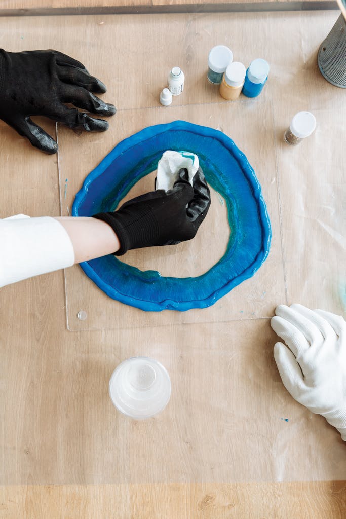 Hands in gloves crafting with resin, creating art on a wooden surface.
