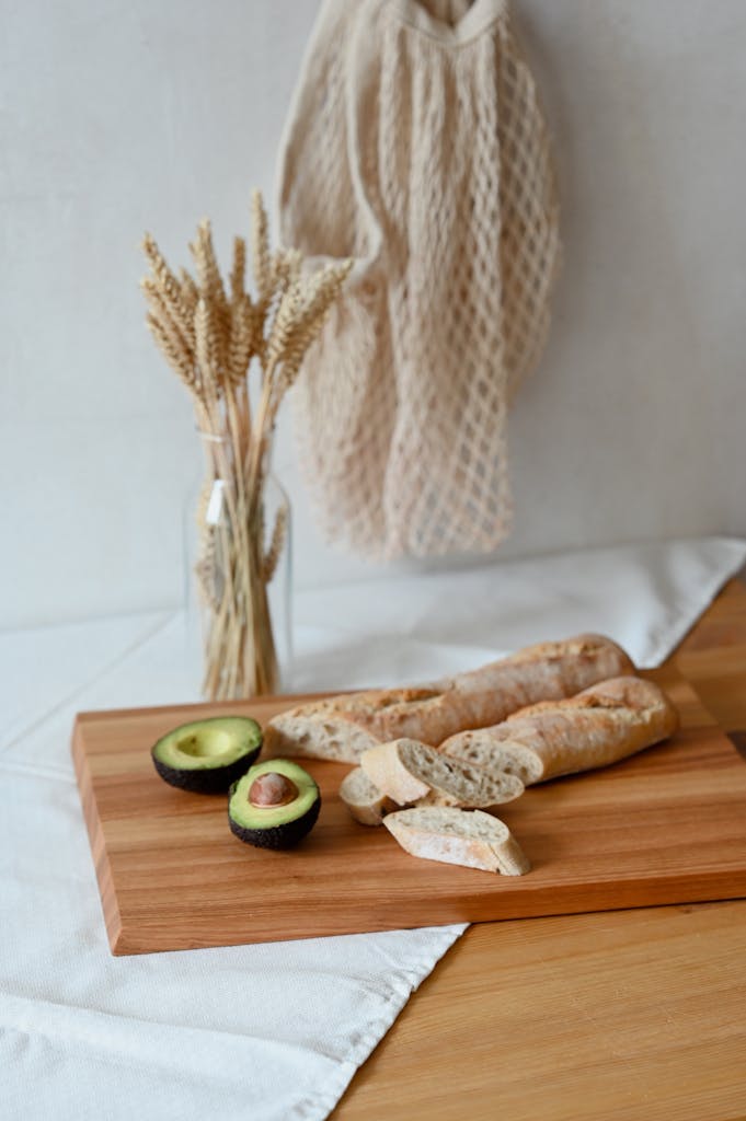 Rustic bread and fresh avocado on a wooden tray with decorative wheat in bottle.