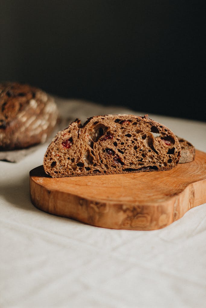 Sliced of tasty cranberry whole wheat bread placed on wooden cutting board on table against black background in light studio