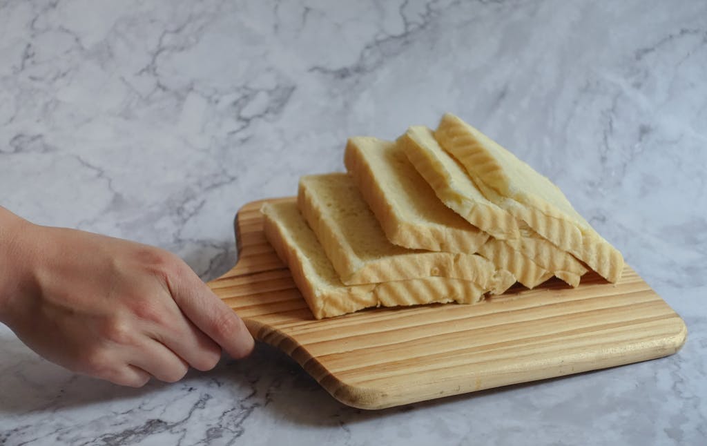Sliced white bread on a wooden board with a hand holding the handle, perfect for bakery ads.