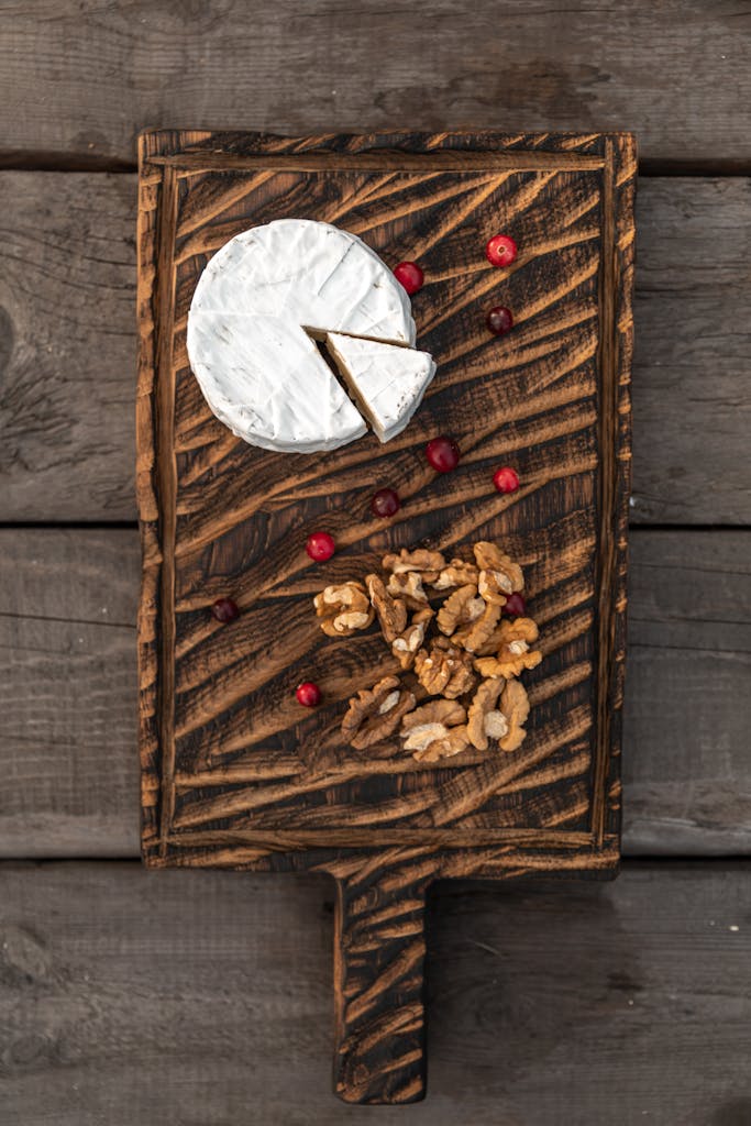 Top view of Brie cheese and walnuts on a wooden board with cranberries, perfect for gourmet food presentations.