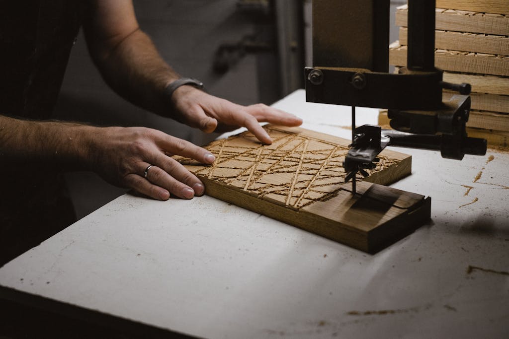 Unrecognizable male master using sharp bandsaw machine while creating pattern on wooden plank in dark professional carpentry with equipment